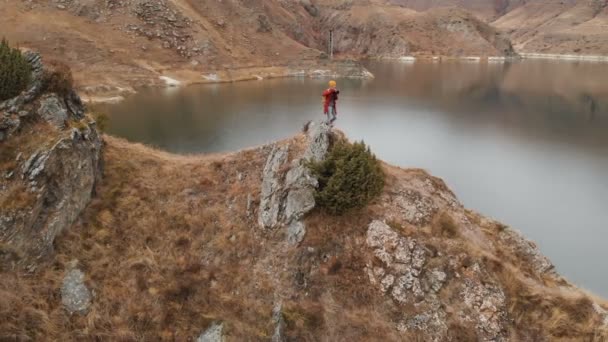 Vista aérea de uma menina em pé sobre uma rocha na margem de um lago, que fotografa a paisagem em sua câmera DSLR. Viagens vídeos — Vídeo de Stock