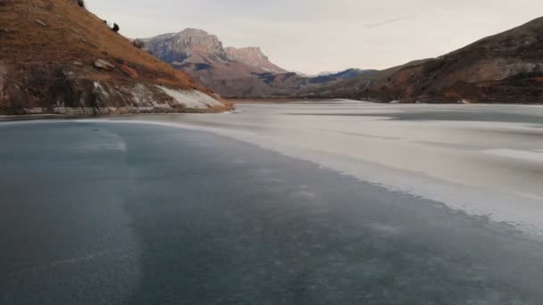 Vista aérea de un vuelo bajo sobre un lago congelado en invierno rodeado por las montañas del Cáucaso después del atardecer a la hora azul — Vídeo de stock