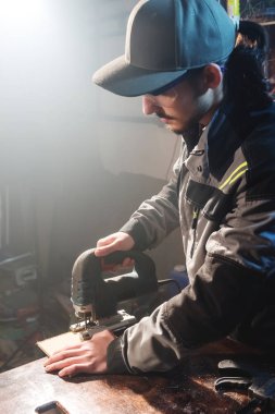 Gri tulum ve gözlük mesleği sakallı genç adam bir marangoz bir elektrikli testere onun ev atölye olarak çalışıyor. Kesme ahşap parçaları