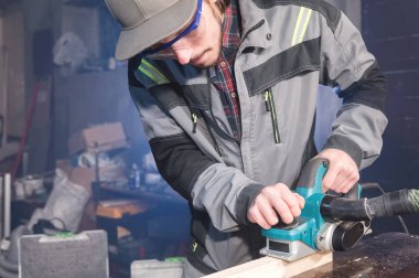 Genç sakallı bir elektrikli uçak talaş emme ile çalışan bir marangoz. Tesviye ve ahşap çubukları zımpara