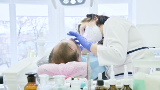 Dentista femenina con un asistente examina la boca de los pacientes de un hombre de edad avanzada. Trabajo profesional clave de un dentista en la clínica dental — Vídeos de Stock