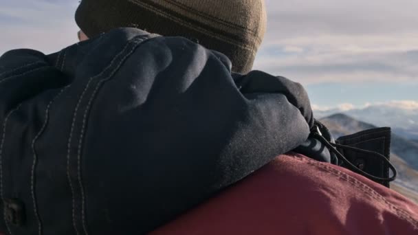 クローズアップ、山の冬の暖かいジャケットと帽子で白人の男の背面のビューは、日没時にエルブルス山を見ています。ヘッドの回転 — ストック動画