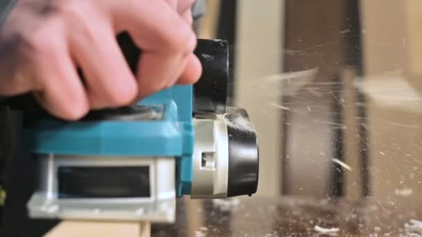 Close-up van een timmerlieden hand werken met een elektrisch vliegtuig in een huis workshop. Afwerking van houten onderdelen in slow motion — Stockvideo
