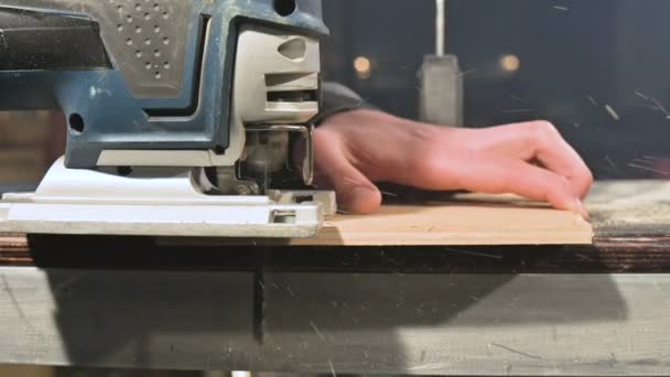 Gran primer plano. Un carpintero cortando una tabla de madera con un rompecabezas eléctrico. Movimiento lento de partículas de polvo y hoja de sierra — Vídeos de Stock