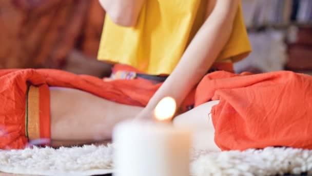 Gros plan une fille entourée de bougies à la maison à la fenêtre médite en position lotus faisant mudra doigts à côté de l'encens aromatique — Video