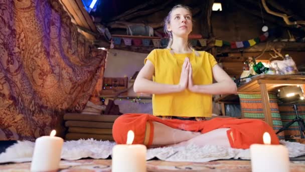 En vacker ung flicka i lösa kläder sitter i ett hantverk rum på en vit päls hud i en Lotus position omgiven av ljus. Meditation andlig tillväxt och vård för din egen hälsa — Stockvideo