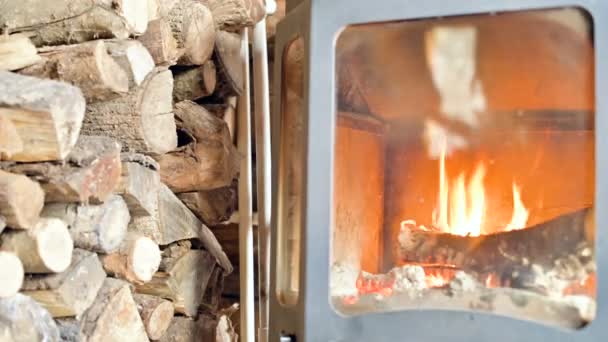 Gros plan de la combustion de bois de chauffage dans un poêle moderne fait maison derrière du verre réfractaire pendant la journée à côté d'une grande pile de bois de chauffage. Énergie respectueuse de l'environnement 