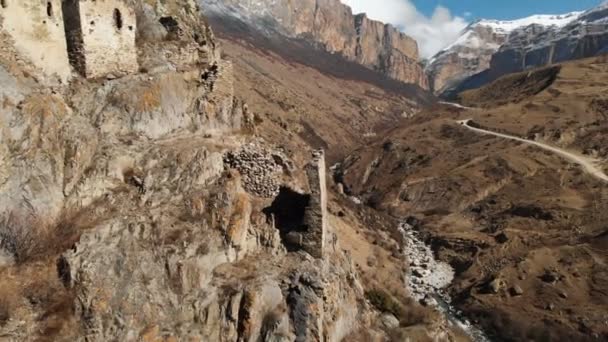 Zříceniny starověkých věží na skále v horách horního Balkarie. Letecký pohled na soutěsku se špinavou silnicí a horskou řekou v kavkazských horách. slunečný den — Stock video