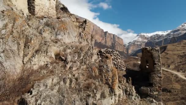 As ruínas das antigas torres sobre uma rocha nas montanhas da Alta Balcária. Vista aérea do desfiladeiro com uma estrada de terra e um rio de montanha nas montanhas do Cáucaso. dia ensolarado — Vídeo de Stock