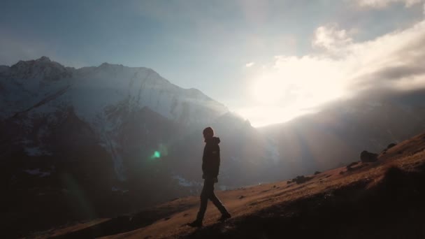 Luchtfoto van een epische shot van een man lopen op de rand van een berg als een silhouet in een prachtige zonsondergang. Silhouet van een man met een baard en een hoed naar beneden de berg op een helling — Stockvideo