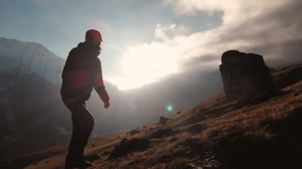 Vista aérea de la épica toma de un hombre caminando en el borde de la montaña como una silueta en una hermosa puesta de sol. Silueta de un hombre con barba y sombrero trepando cuesta arriba — Vídeos de Stock