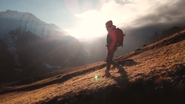 Εναέρια θέα ενός επική βολή ενός κοριτσιού που περπατάει στην άκρη ενός βουνού ως σιλουέτα σε ένα όμορφο ηλιοβασίλεμα. Σιλουέτα ενός κοριτσιού σε ένα καπέλο με ένα σακίδιο που κατεβαίνει από το βουνό σε μια βουνοπλαγιά — Αρχείο Βίντεο