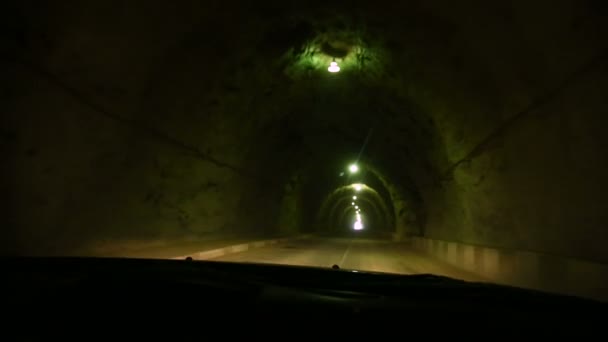 Vista a través del parabrisas del coche. El coche atraviesa un túnel hecho en una roca con poca luz y una carretera rural. Caminos de montaña del Cáucaso — Vídeo de stock