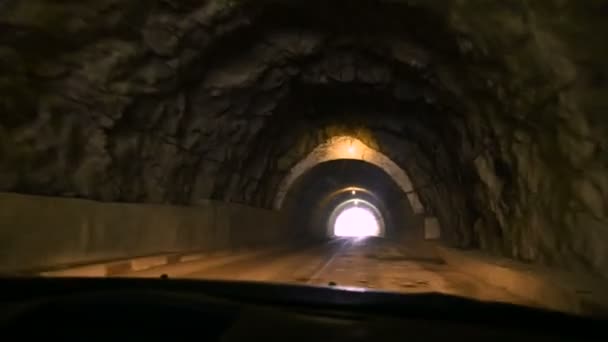 View through the windshield of the car. The car rides through a tunnel made in a rock with dim lighting and a country road. Caucasus mountain roads — Stock Video