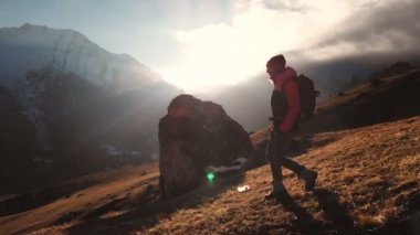 Güzel bir günbatımı bir siluet olarak bir dağın kenarında yürüyen bir kızın epik bir çekim havadan görünümü. Bir şapkalı bir kızın silüeti, dağa bir dağın aşağısında bir sırt çantası ile geliyor.