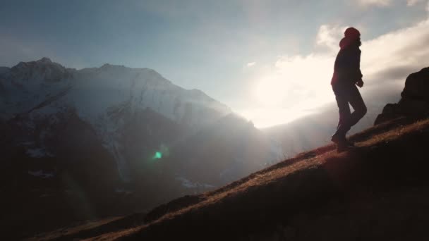 Vista aérea de la épica toma de un hombre caminando en el borde de la montaña como una silueta en una hermosa puesta de sol. Silueta de un hombre con barba y sombrero trepando cuesta arriba — Vídeo de stock
