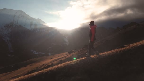 Πολύ μακριά shot εναέρια θέα ενός επική βολή ενός κοριτσιού που περπατάει στην άκρη ενός βουνού ως σιλουέτα σε ένα όμορφο ηλιοβασίλεμα. Σιλουέτα ενός κοριτσιού σε ένα καπέλο που κατεβαίνει από το βουνό σε μια βουνοπλαγιά — Αρχείο Βίντεο
