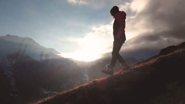 Vista aérea de una foto épica de una niña caminando en el borde de una montaña como silueta en una hermosa puesta de sol. Silueta de una chica con un sombrero bajando por la montaña en una ladera — Vídeos de Stock