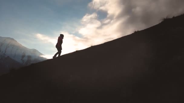 Very long shot Aerial view of epic shot of a girl walking on the edge of the mountain as a silhouette in a beautiful sunset. Silhouette of a girl in a hat climbing uphill — Stock Video