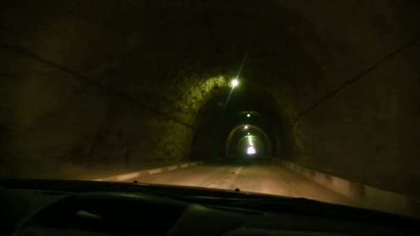 Vista a través del parabrisas del coche. El coche atraviesa un túnel hecho en una roca con poca luz y una carretera rural. Caminos de montaña del Cáucaso — Vídeo de stock