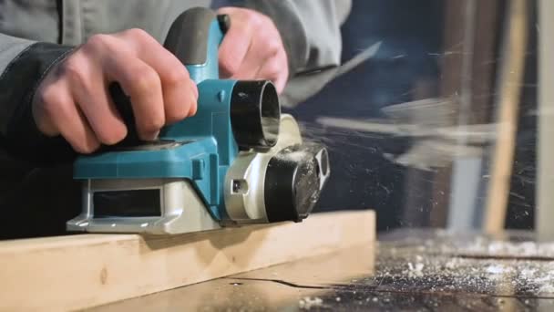 Close-up van een timmerlieden hand werken met een elektrisch vliegtuig in een huis workshop. Afwerking van houten onderdelen in slow motion — Stockvideo