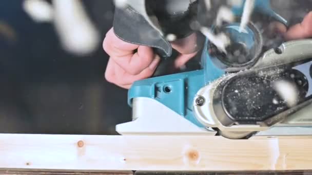 Close-up van een timmerlieden hand werken met een elektrisch vliegtuig in een huis workshop. Afwerking van houten onderdelen in slow motion — Stockvideo