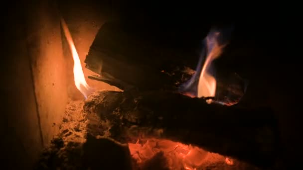 Close-up de lenha mal queimada com carvão em um moderno fogão doméstico atrás de um vidro refratário à noite. Chave baixa. Movimento perto do fogo com a câmara a rodar. Energia ecológica — Vídeo de Stock