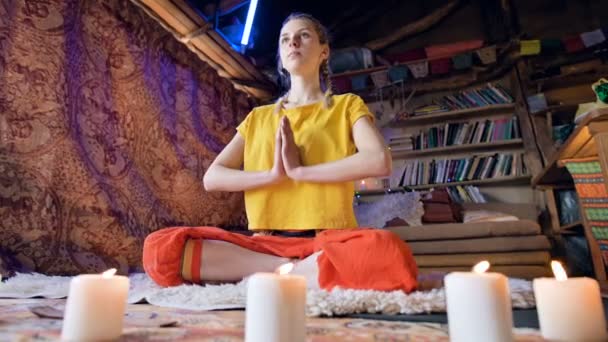 En vacker ung flicka i lösa kläder sitter i ett hantverk rum på en vit päls hud i en Lotus position omgiven av ljus. Meditation andlig tillväxt och vård för din egen hälsa — Stockvideo