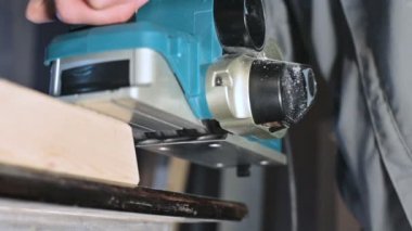 Büyük yakın çekim. Bir marangoz, elektrikli düzlemde ahşap bir tahta kesiyor. Toz parçacıklarının ve testere bıçağının yavaş hareketi