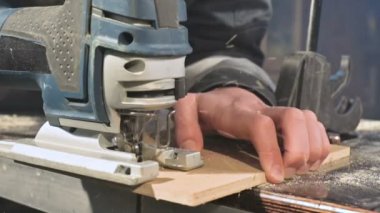 Büyük yakın çekim. Bir marangoz bir elektrikli jigsaw ile ahşap tahta kesme. Toz parçacıklarının ve testere bıçağının yavaş hareketi