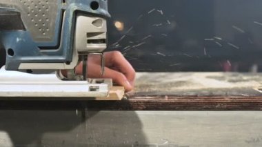 Büyük yakın çekim. Bir marangoz bir elektrikli jigsaw ile ahşap tahta kesme. Toz parçacıklarının ve testere bıçağının yavaş hareketi