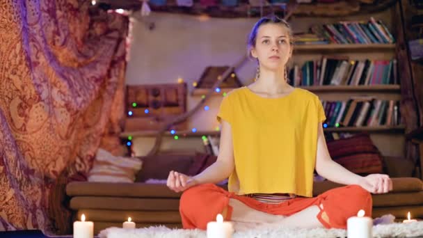 緩い服の深刻な美しい若い女の子は、キャンドルに囲まれた蓮の位置に白い毛皮の皮の上の工芸室に座っています。瞑想の精神的な成長とあなた自身の健康のケア — ストック動画