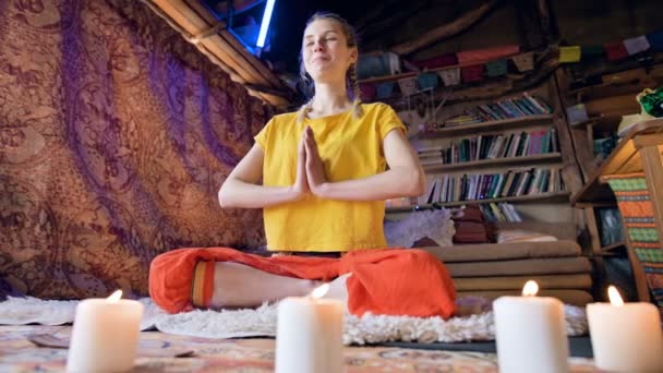 En skrattande vacker ung flicka i lösa kläder sitter i ett hantverk rum på en vit päls hud i en Lotus position omgiven av ljus. Meditation andlig tillväxt och vård för din egen hälsa — Stockvideo