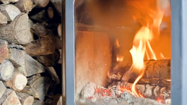Aproape de arderea lemnului de foc într-o sobă modernă făcută acasă în spatele sticlei refractare în timpul zilei, lângă o grămadă mare de lemn de foc. Energie ecologică — Videoclip de stoc