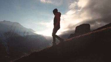 Uzun atış güzel bir gün batımında bir siluet olarak bir dağın kenarında yürüyen bir kızın epik bir çekim havadan görünümü. Bir şapkalı bir kızın silüeti Dağın aşağısında, dağa geliyor.