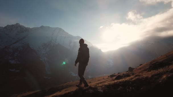 Luchtfoto van een epische shot van een man lopen op de rand van een berg als een silhouet in een prachtige zonsondergang. Silhouet van een man met een baard en een hoed naar beneden de berg op een helling — Stockvideo