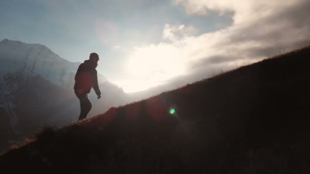 Luchtfoto van epische shot van een man lopen op de rand van de berg als een silhouet in een prachtige zonsondergang. Silhouet van een man met een baard en het dragen van een hoed klimmen bergop — Stockvideo