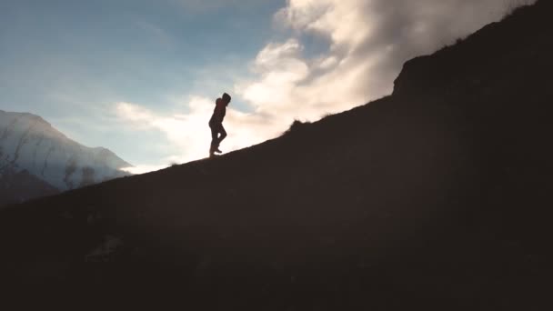 Vista aérea de una foto épica de una niña caminando en el borde de la montaña como una silueta en una hermosa puesta de sol. Silueta de una chica en un sombrero trepando cuesta arriba — Vídeos de Stock