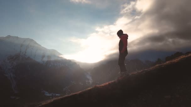 Vista aérea de una foto épica de una niña caminando en el borde de una montaña como silueta en una hermosa puesta de sol. Silueta de una chica con un sombrero bajando por la montaña en una ladera — Vídeo de stock