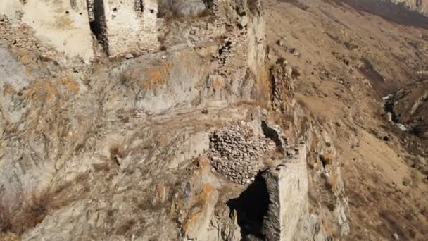 Τα ερείπια των αρχαίων πυργίσων σε ένα βράχο στα βουνά του άνω Βαλάρια. Εναέρια θέα του φαραγγιού με χωματόδρομο και ορεινό ποταμό στα βουνά του Καυκάσου. ηλιόλουστη μέρα — Αρχείο Βίντεο