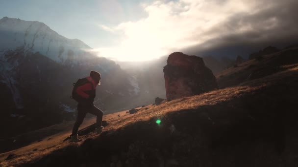 Luchtfoto van epische shot van een meisje lopen op de rand van de berg als een silhouet in een prachtige zonsondergang. Silhouet van een meisje in een hoed met een rugzak klimmen bergop — Stockvideo