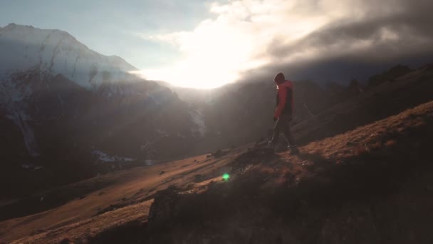 Vista aérea de una foto épica de una niña caminando en el borde de una montaña como silueta en una hermosa puesta de sol. Silueta de una chica con un sombrero bajando por la montaña en una ladera — Vídeo de stock