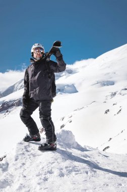 Büyüme Portre sakallı erkek kayakçı kar kaplı Kafkas dağlarının arka plan karşı yaşlı. Omzunda kayak googles maskesi ve kask kayaklar giyen yetişkin bir adam dağlara bakıyor. Kayak merkezi konsepti