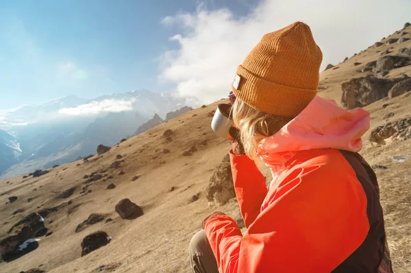 Close-up Retrato de uma menina bonita em um chapéu e óculos de sol com uma caneca de café ou chá enquanto sentado em uma pedra nas montanhas. O conceito de turismo e recreação nas montanhas — Fotografia de Stock