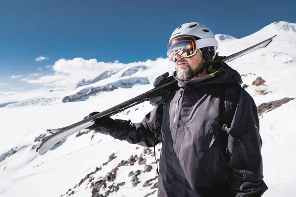 Yakın çekim Portre sakallı erkek kayakçı dağların arka planına karşı yaşlı. Omzunda kayak googles maskesi ve kask kayaklar giyen yetişkin bir adam dağlara bakıyor. Kayak merkezi konsepti