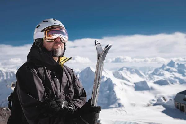 Retrato atleta esquiador em capacete e máscara de esqui contra as montanhas cobertas de neve de uma estância de esqui com um reflexo das montanhas caucasianas na máscara — Fotografia de Stock