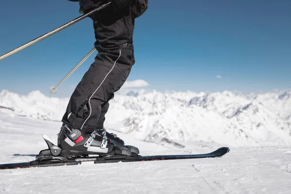 在阳光明媚的日子里，在白雪覆盖的高加索山脉的背景下，滑雪者穿着滑雪靴的特写镜头进入滑雪板。冬季运动理念 — 图库照片