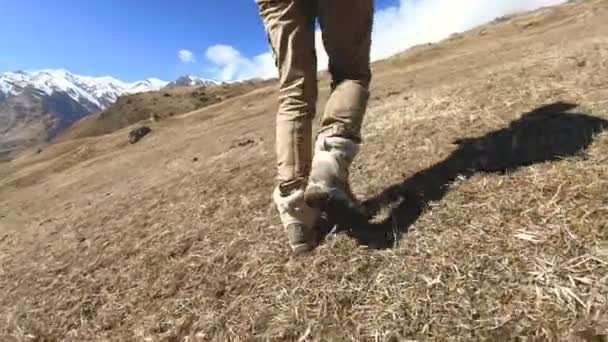 Ноги дівчини мандрівника йдуть в гору на тлі засніжених вершин в сонячний день — стокове відео
