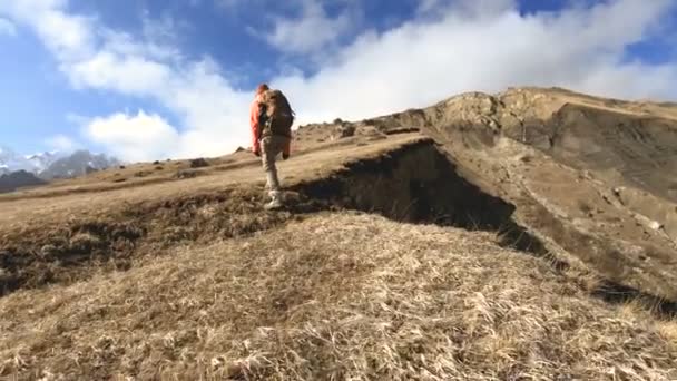 Feliz fotógrafa viajera en gafas de sol con una cámara y una mochila va cuesta arriba sobre un fondo de picos nevados en un día soleado — Vídeos de Stock