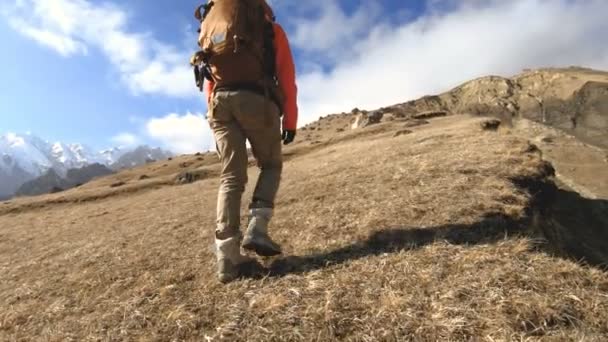 Gelukkige reiziger meisje fotograaf in zonnebril met een camera en een rugzak gaat bergopwaarts op een achtergrond van besneeuwde toppen op een zonnige dag — Stockvideo